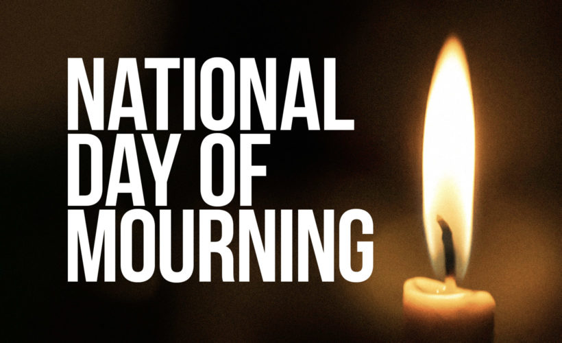 Lit candle on a dark background with words National Day of Mourning
